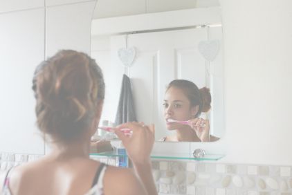 Photo of a woman in her bathroom brushing her teeth in front of a mirror.