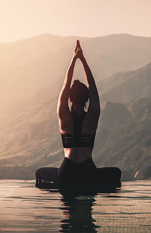 Femme de dos sur l'eau pratiquant du yoga en regardant les montagnes