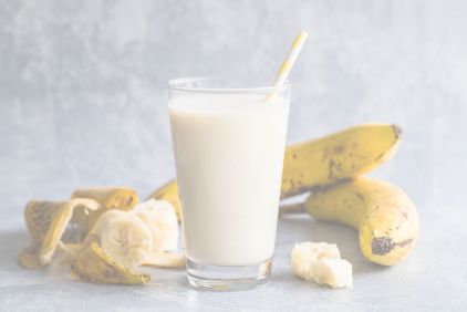 Photo of a glass filled with bilva banana milkshake with bananas in the background